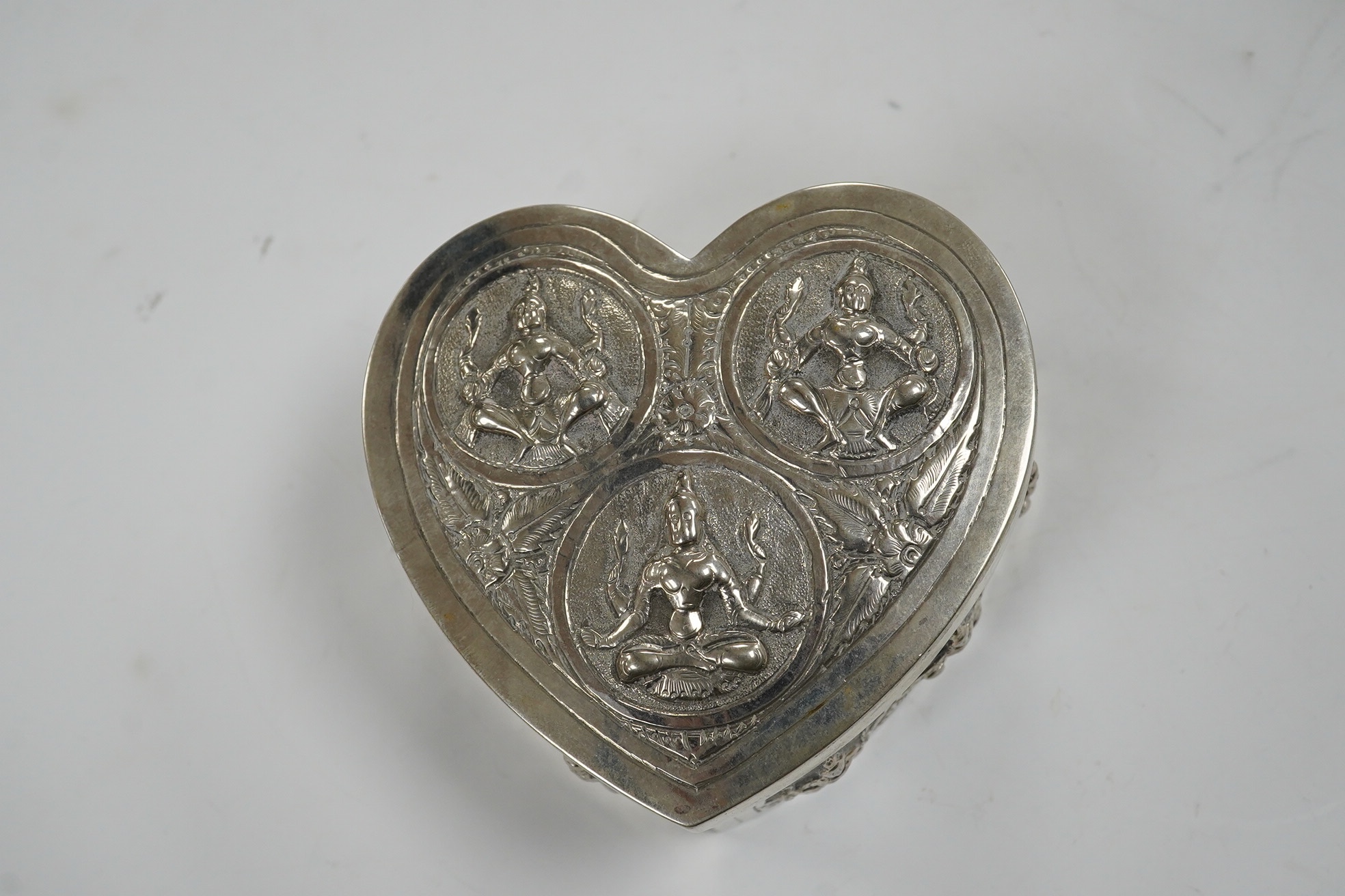 An Indian embossed white metal heart shaped trinket box and cover, width 85mm, 120 grams. Condition - fair
